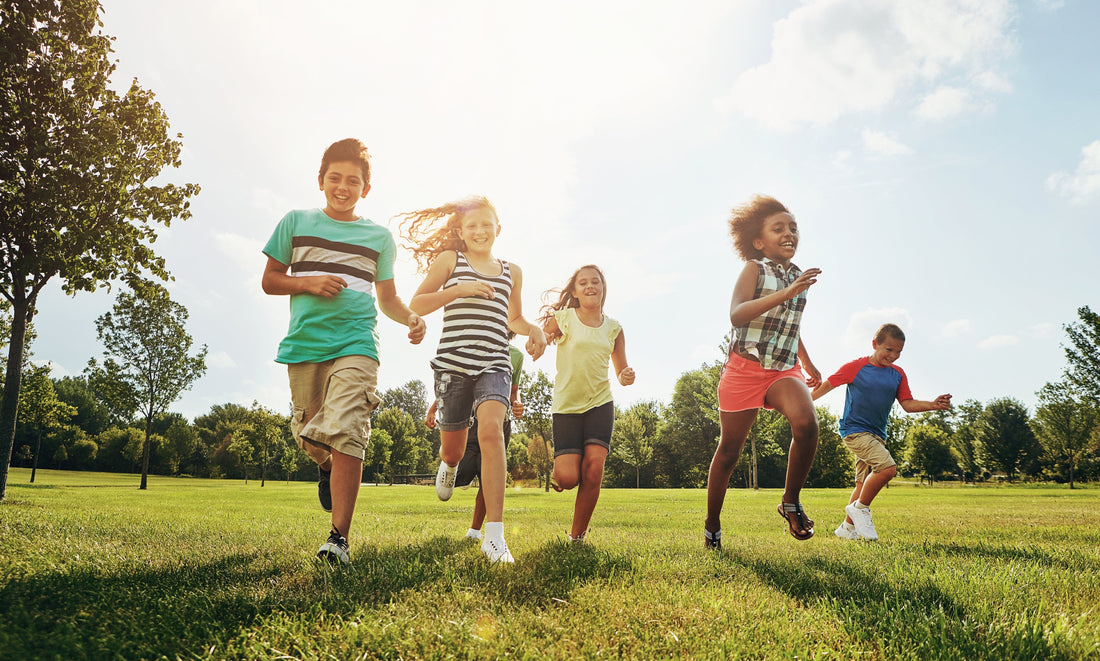 Five children in summer clothes running through a grassy field under bright sunlight.