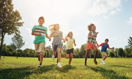 Five children in summer clothes running through a grassy field under bright sunlight.