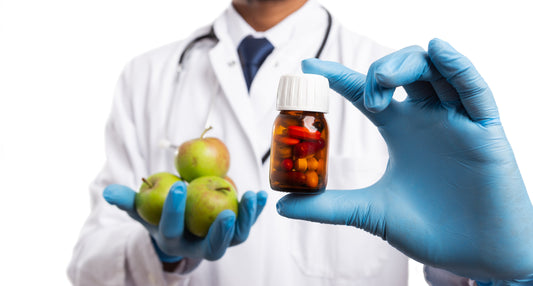 A doctor in a lab coat with a stethoscope holding a bottle of pills in one hand and apples in the other