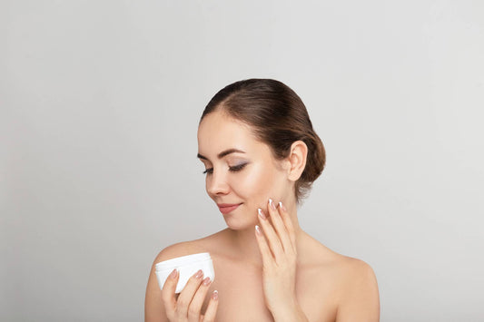 A young woman with smooth skin applying face cream while looking down at the product jar, symbolizing beauty, internal wellness, and skin support.