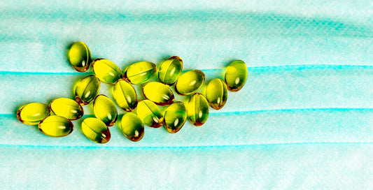 Yellow vitamin or fish oil capsules scattered across a light blue surgical mask, symbolizing immune support and general wellness in the context of public health.