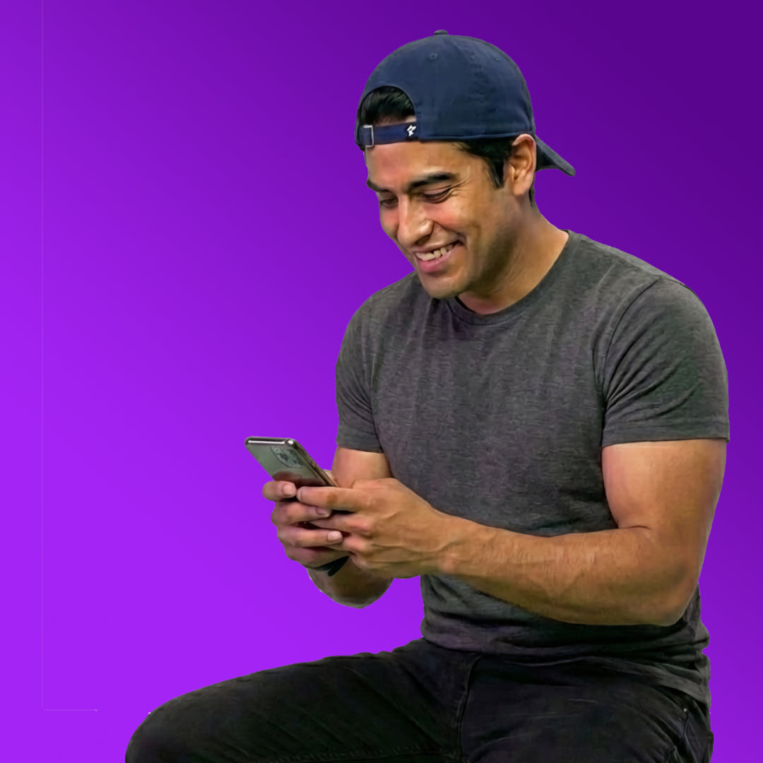 Man wearing a dark cap and gray t-shirt using a smartphone on a purple background